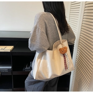 Detail of white textured leather tote bag with brown plush bear and ribbon accessory