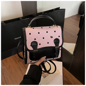 Detailed close-up of pink polka dot backpack featuring black leather straps and golden buckles