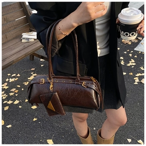 Detail of dark brown crinkled patent leather bag with gold buckles and mini charm