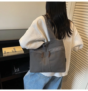 Detail of dark grey canvas tote bag featuring double front zipper pockets and wide shoulder strap
