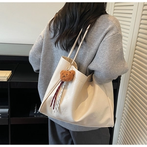 Detail of off-white faux leather tote bag with soft texture and plush bear charm