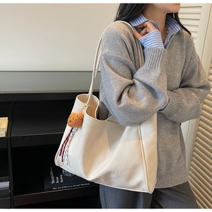 Detailed view of creamy white leather tote bag featuring a cute brown bear charm