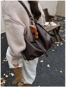 Detail of dark brown leather tote bag with a small bear pendant in an autumn outdoor setting