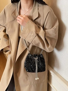 Fashionable black quilted bucket bag with chain strap and pearl details on a trench coat