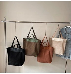 Detail view of four large tote bags in black, green, brown, and beige hanging on a rack