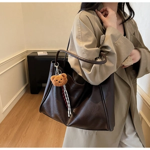 Detail of dark brown faux leather tote bag with plush bear charm on minimalist background