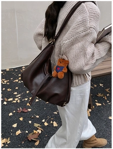 Detail of dark brown faux leather dumpling bag with bear charm and adjustable strap
