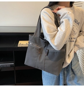 Detail of dark grey canvas tote bag with front zip pockets worn by a model