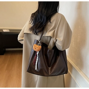 Detail of deep brown faux leather tote bag with cute bear charm worn with beige trench coat