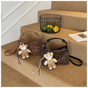 Detail of leopard print crossbody bag with plush bear charm on warm carpet steps