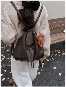 Detail of dark brown leather hobo bag with fringe zipper and cute teddy bear charm accessory