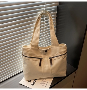 Detail of cream canvas tote bag showing front zip pockets and smooth magnetic snap closure