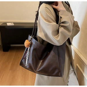 Detail of a dark coffee leather tote bag with a brown plush bear and striped ribbon charm