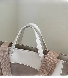Detail of the stitching on dual handles and wide woven shoulder strap of the tote bag