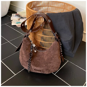 Détail du sac hobo en daim marron foncé avec bandoulière à œillets et breloque tissée