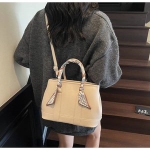 Chic beige lychee leather tote bag with silk scarf detail worn as a shoulder bag
