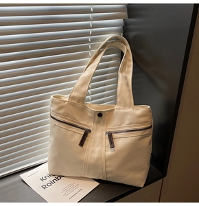Detail of off-white canvas tote bag featuring double front zippers and natural light shadows