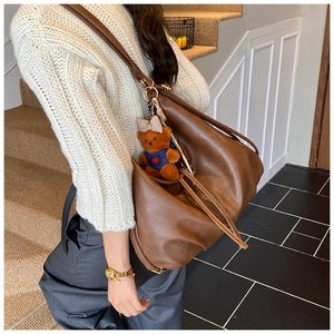 Brown vintage pleated dumpling bag shown on shoulder with cute bear keychain accessory