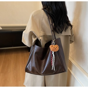 Detail view of large dark brown tote bag with plush bear charm on a beige coat