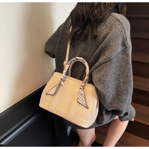 Detail of beige bucket bag featuring a silk scarf wrap handle and vertical stitching