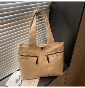 Detail of cream canvas tote bag with dual zipper pockets and brown leather pulls