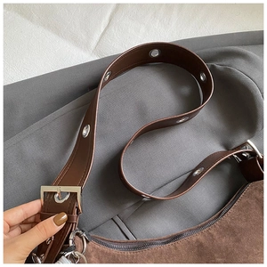 Détail macro du sac en daim marron foncé avec œillets métalliques et boucle de sangle