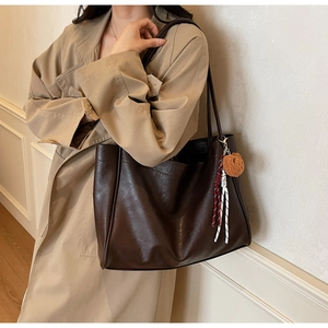 Detail of deep brown leather tote bag with plush bear charm and rope accessory worn with trench coat