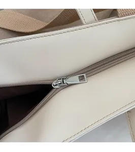 Detailed close-up of smooth silver metal zipper and neat stitching on off-white tote bag
