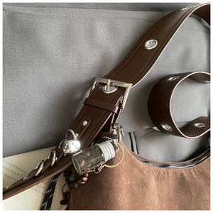 Détail du sac hobo en daim marron foncé avec œillets argentés et breloques vintage