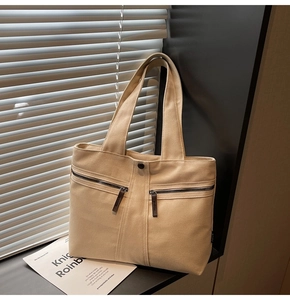 Close-up of beige canvas tote bag with front zipper pockets and leather pull tabs