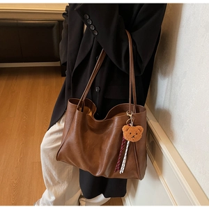 Close-up of brown textured tote bag featuring a cute plush bear charm on the strap