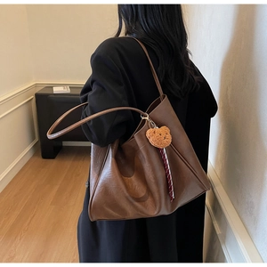 Close-up of brown leather tote bag with plush bear charm and natural texture