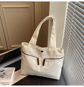 Detail of off-white canvas tote bag with dual front zipper pockets and top handles