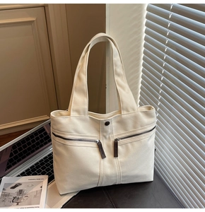 Macro detail of creamy white canvas tote bag with brown leather zipper pulls and front pockets