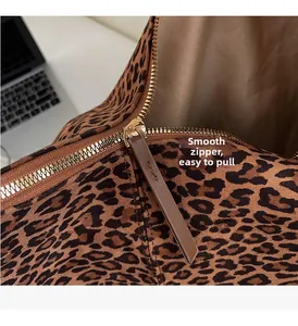 Close-up of smooth gold metal zipper and brown leather pull on leopard print suede bag