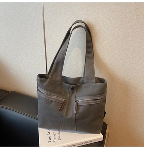 Detail of dark grey canvas tote bag with diagonal zipper pockets on leather sofa