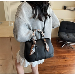 Black pebble leather bucket bag with silk scarf on handle worn by model in casual style