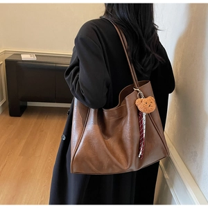 Detail view of a large brown tote bag with a plush bear charm and striped strap