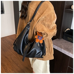 Detail of a large black glossy hobo bag with a cute brown teddy bear pendant on strap