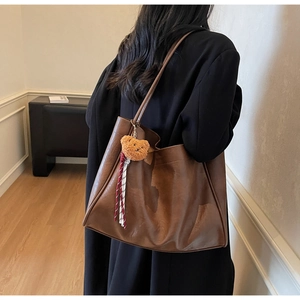 Detail of a brown tote bag featuring a plush bear pendant with a plaid ribbon on smooth leather