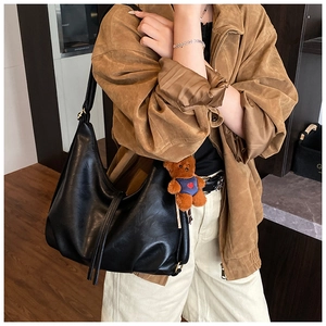 Detail of black pleated tote bag with plush bear charm and wide shoulder strap