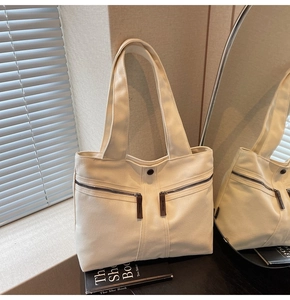 Detail of off-white canvas tote bag featuring double front zippers and wide shoulder straps