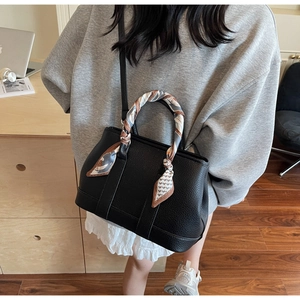 Detail of black pebbled leather bucket bag featuring a decorative geometric silk scarf handle