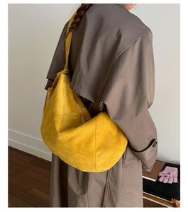 Detail of yellow suede crescent bag with knot shoulder strap worn over a brown coat