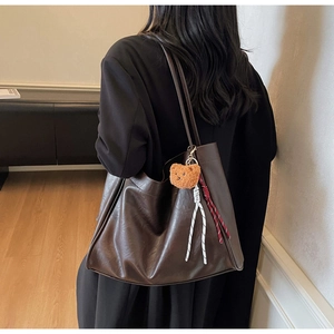 Detail of deep brown leather tote bag with plush bear charm and sleek shoulder straps