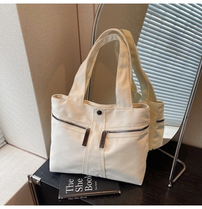 Close-up of cream canvas tote bag featuring dual front zipper pockets and leather pulls