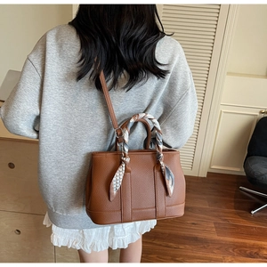 Brown litchi grain leather tote bag with silk scarf handle detail worn by model
