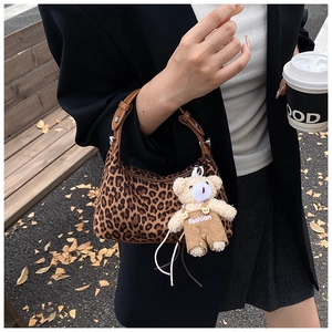 Detail of leopard print handbag featuring a plush bear charm and brown leather handle