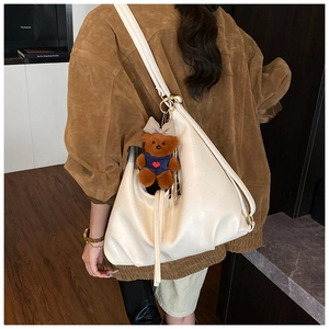 Detail of off-white oversized hobo bag featuring a cute plush bear charm and soft pleats