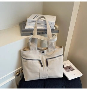 Detail view of beige canvas tote bag with front diagonal zippers and metal snap button
